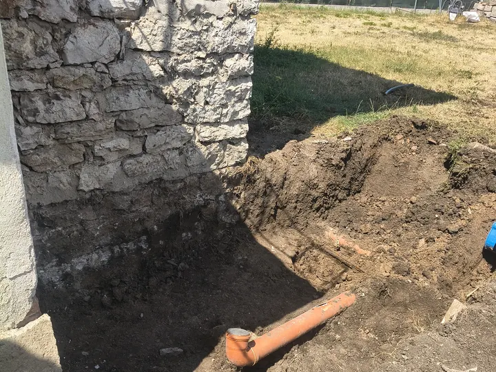 Изкоп за канализационна тръба с коляно до каменна стена